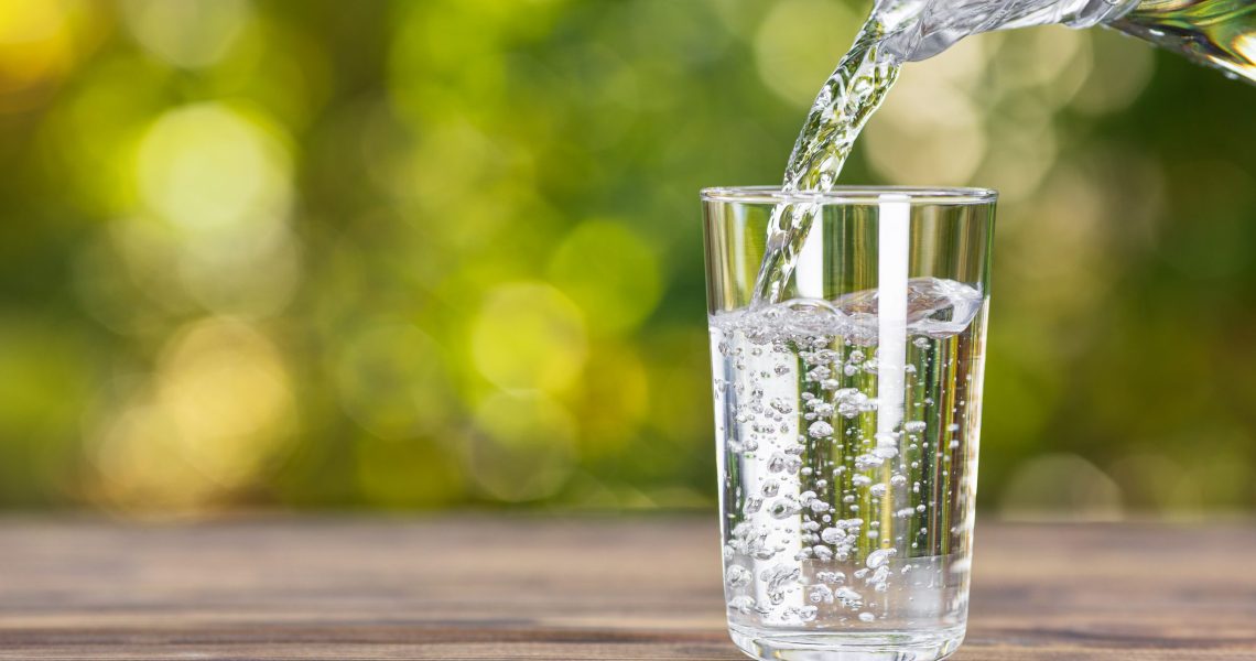 Water,From,Jug,Pouring,Into,Glass,On,Wooden,Table,Outdoors