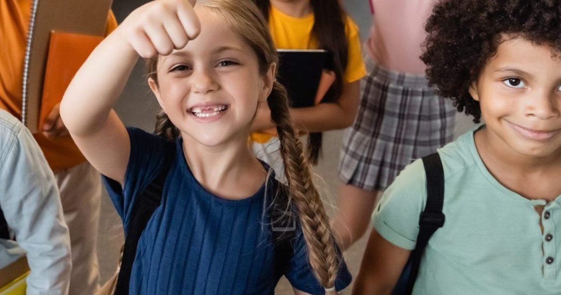 Cheerful,Multicultural,Schoolchildren,Showing,Thumbs,Up,In,School,Corridor